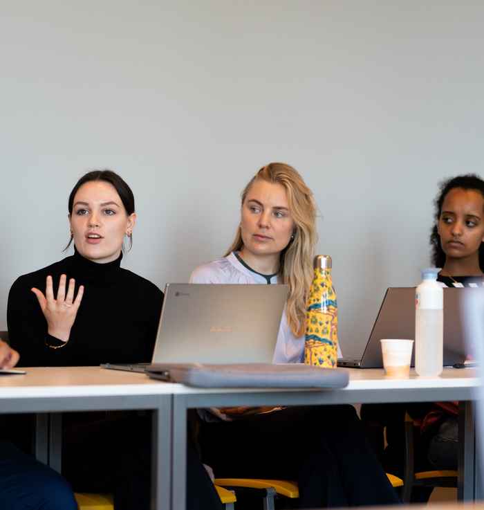 Drie vrouwelijke studenten op een rij achter een bureau waarvan 1 met handgebaren praat